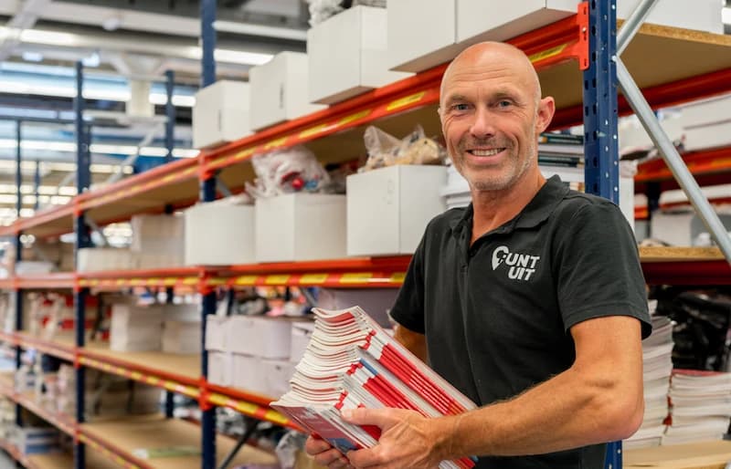 Een werknemer in het magazijn van Punt-Uit die een stapel boeken vasthoudt